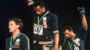 In this Oct. 16, 1968, file photo, United States gold medalist Tommie Smith, center, and bronze medalist John Carlos, right, stare downward while extending their gloved hands skyward in racial protest alongside Australian silver medalist Peter Norman during the playing of "The Star Spangled Banner."