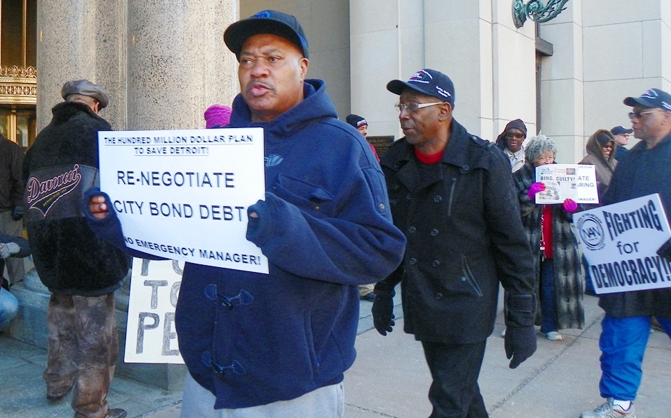Protester outside EM press conference Marcy 14, 2013 calls on city to confront banks.