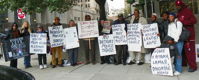 Families display signs outside courthouse (l to r) Gabrielle and Dominique Harrison, Oct. 22 protester, Khalid Fareed, Roberto Guzman, unnamed, Gary of Oct. 22nd, Herman Vallery, Cornell Squires, unnamed, daughter of Taminko-Sanford-Tilmon at her left, Jermaine Tilmon, with grandson Omari.