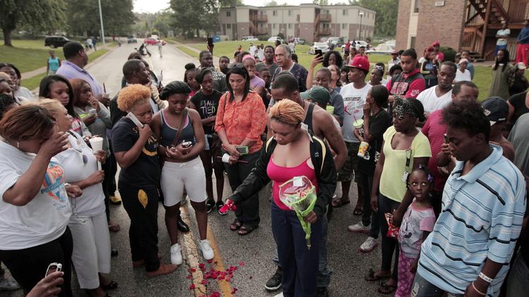 (Huy Mach / St. Louis Post-Dispatch) Lesley McSpadden, center, drops rose petals on the bloodstains from her son, Michael Brown, 18, who was shot dead by police in Ferguson, Mo.