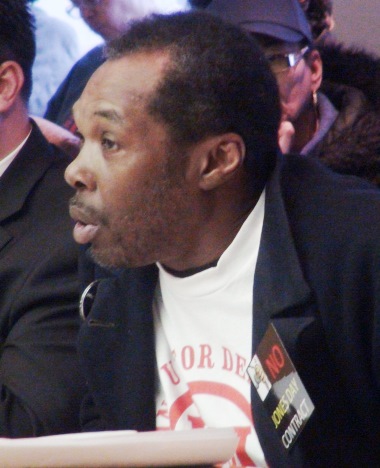 Speaker at Detroit City Council, wearing "NO JONES DAY" opposes hiring of firm April 9, 2013. A strong campaign was waged by hundreds of Detroiters to stop the contract. Jones Day previously represented the State of Michigan to engineer the bankruptcy.