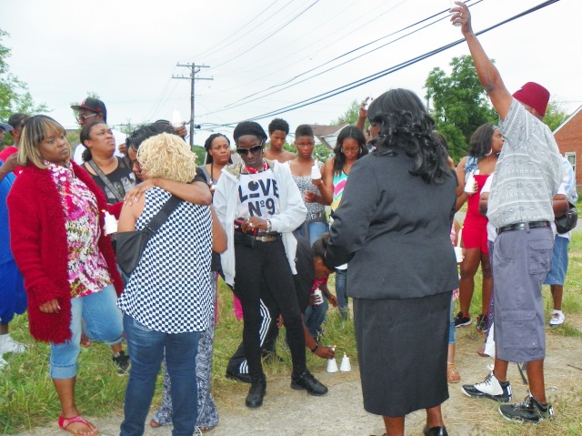 Family, neighbors console Alisha Jackson, being hugged by woman in blue-checked shirt, at vigil.