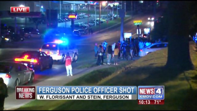 Ferguson police set up a staging area near scene of Mike Brown's shooting after cop shot; the cop was shot over 2 miles away at the Ferguson Community Center. Confrontations between bystanders and police resulted at this scene.