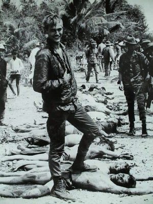 U.S. soldier grins over bodies of Vietnamese patriots killed defending their country.