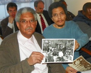 Detroit retiree Walter Knall, historian Paul Lee hold up photo depicting historic rally in Detroit during consent agreement hearings. Pugh ordered police to remove Lee from chambers.